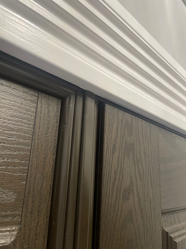 The top latch corner of a closed and latched entry door. The slab stands out past the frame at the head instead of sealing against the weatherstrip. UTS ServicePros field photo.